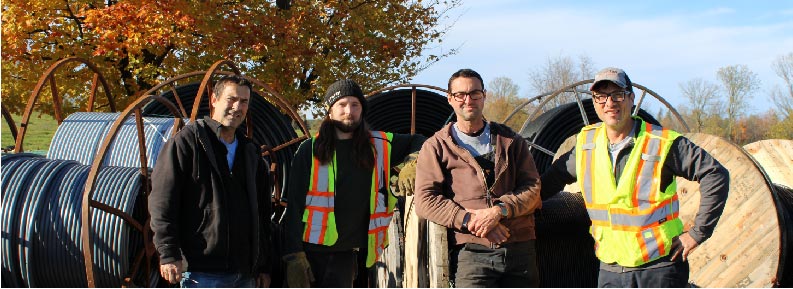 Our VP of construction and operations and three field technicians posing for the camera in front of spools of fibre in Clayton.