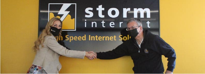 Angella Goran and Birket Foster shaking hands, posing for the camera, in front of a Storm Internet sign inside the Ottawa office.